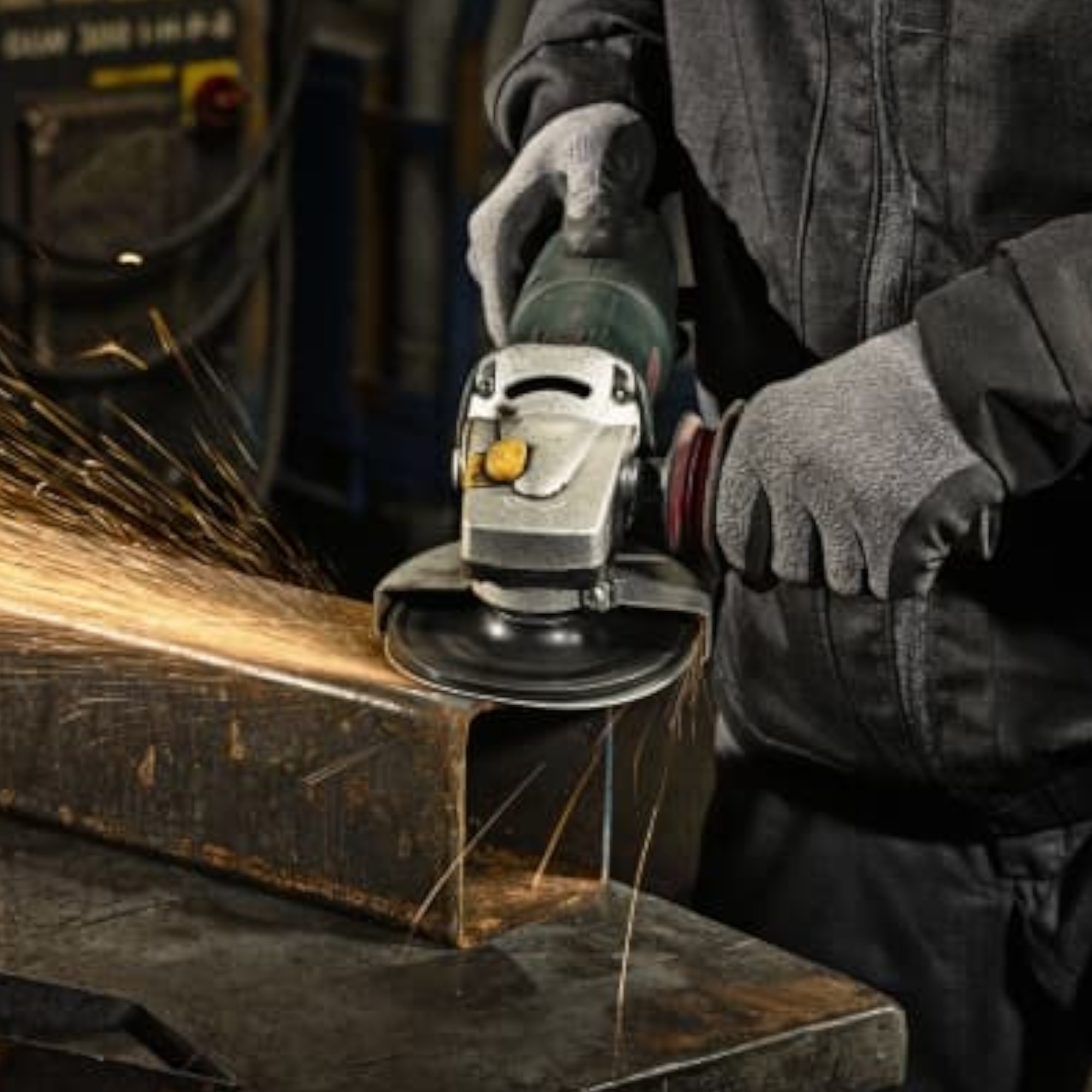 Eine Person trägt Handschuhe und benutzt eine Schleifmaschine, um ein Metallstück zu bearbeiten. Funken fliegen vom Metall weg, während die Maschine in Betrieb ist. Der Fokus liegt auf der Arbeit an dem Metall.