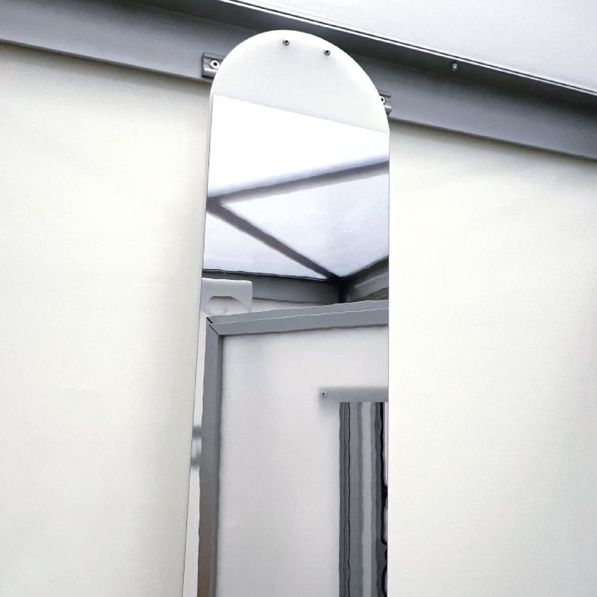 Ovaler, hoher Wandspiegel an grauer Wand in heller, schlichter Umgebung mit reflektierendem Lichteffekt